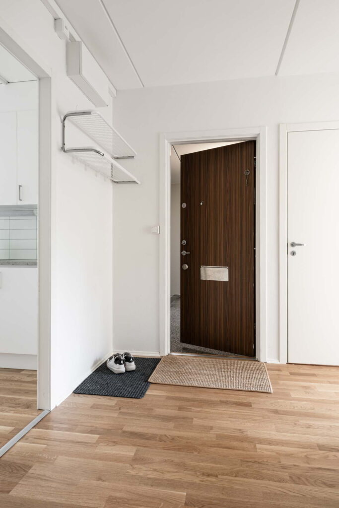 Hall i lägenhet med trägolv, hatthylla och säkerhetsdörr.